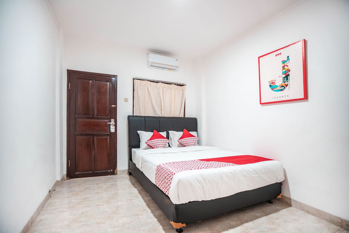 A bedroom with a bed, a door, an air conditioner, and a wall-mounted picture.