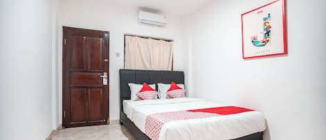 A bedroom with a bed, a door, an air conditioner, and a wall-mounted picture.