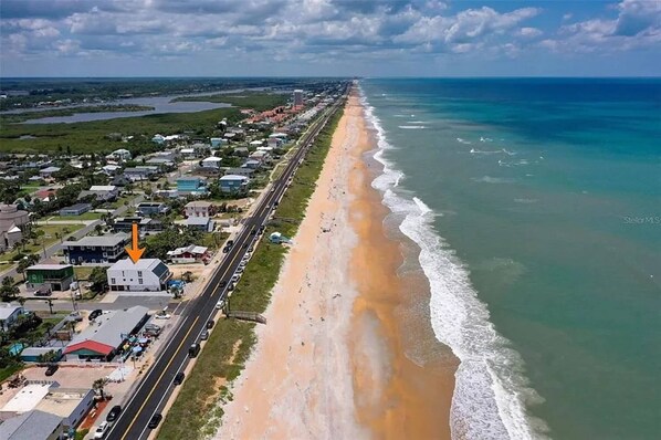 A coastal road with a beach on one side and a residential area on the other.