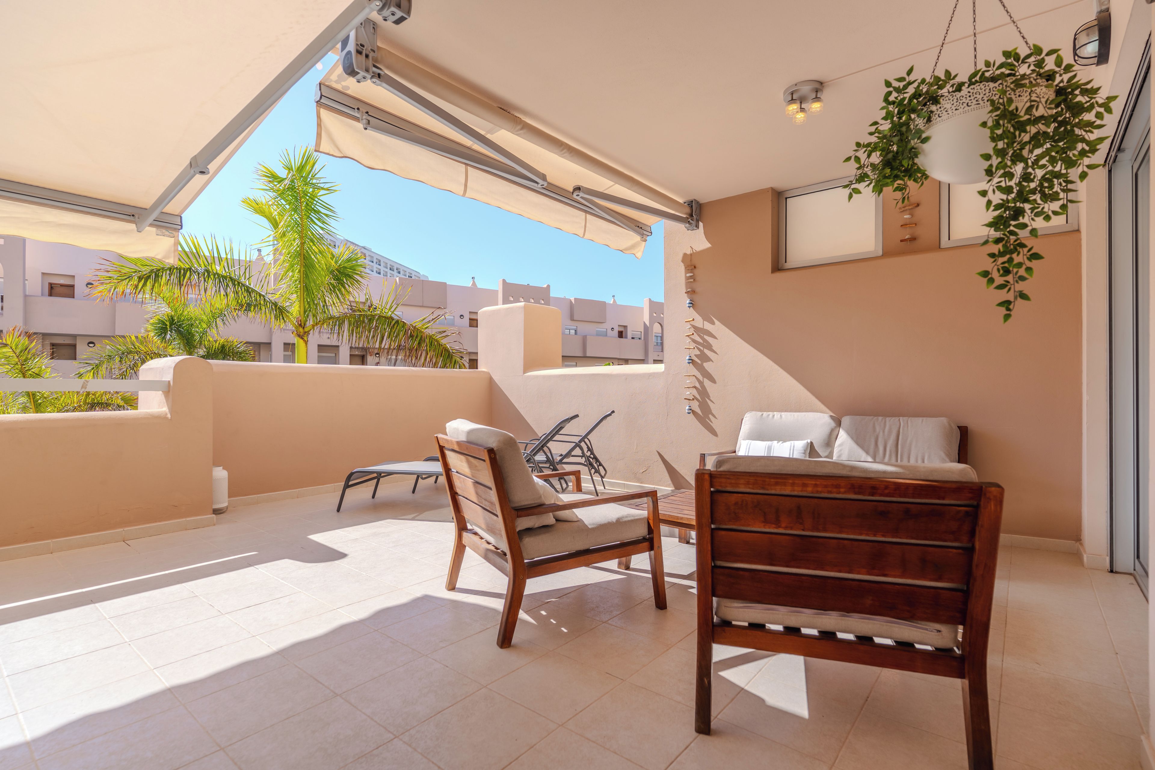 Un balcone con una sedia di legno, un tavolino e una pianta pensile.