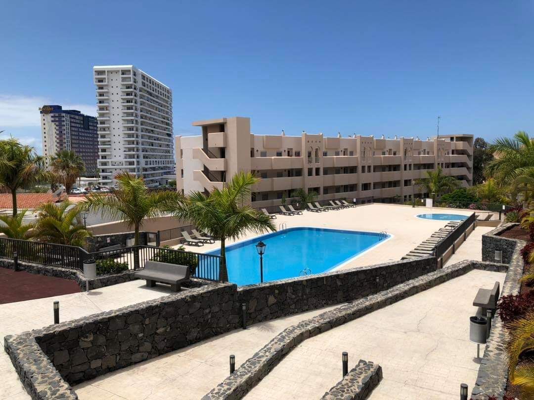 A hotel with a swimming pool, palm trees, and a view of a tall building.