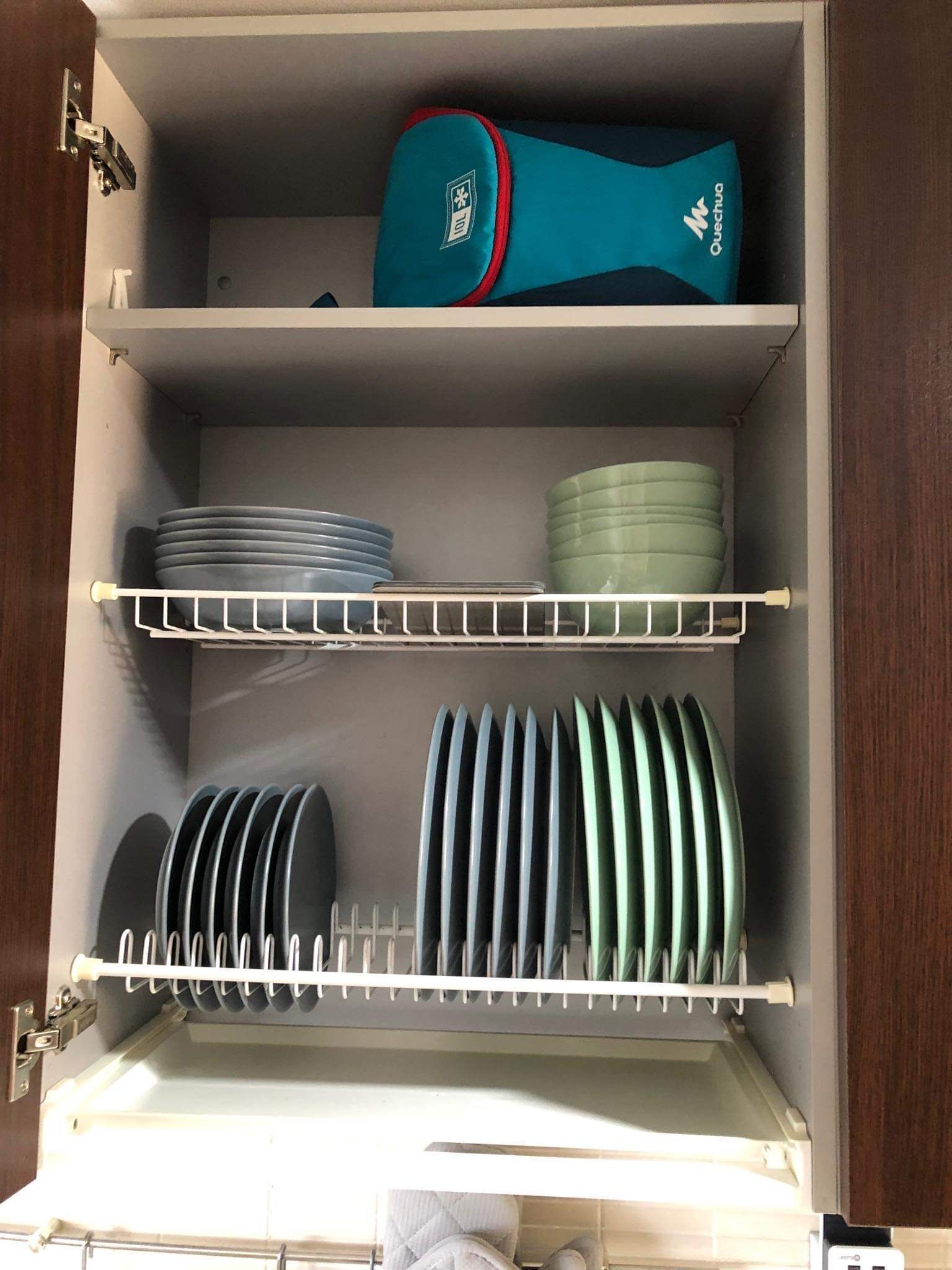 A kitchen cabinet with shelves holding plates, bowls, and a blue container.