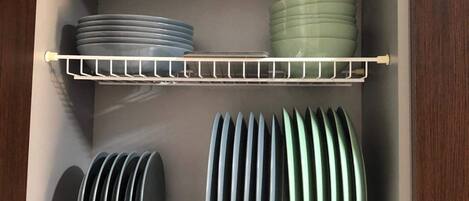 A kitchen cabinet with shelves holding plates, bowls, and a blue container.
