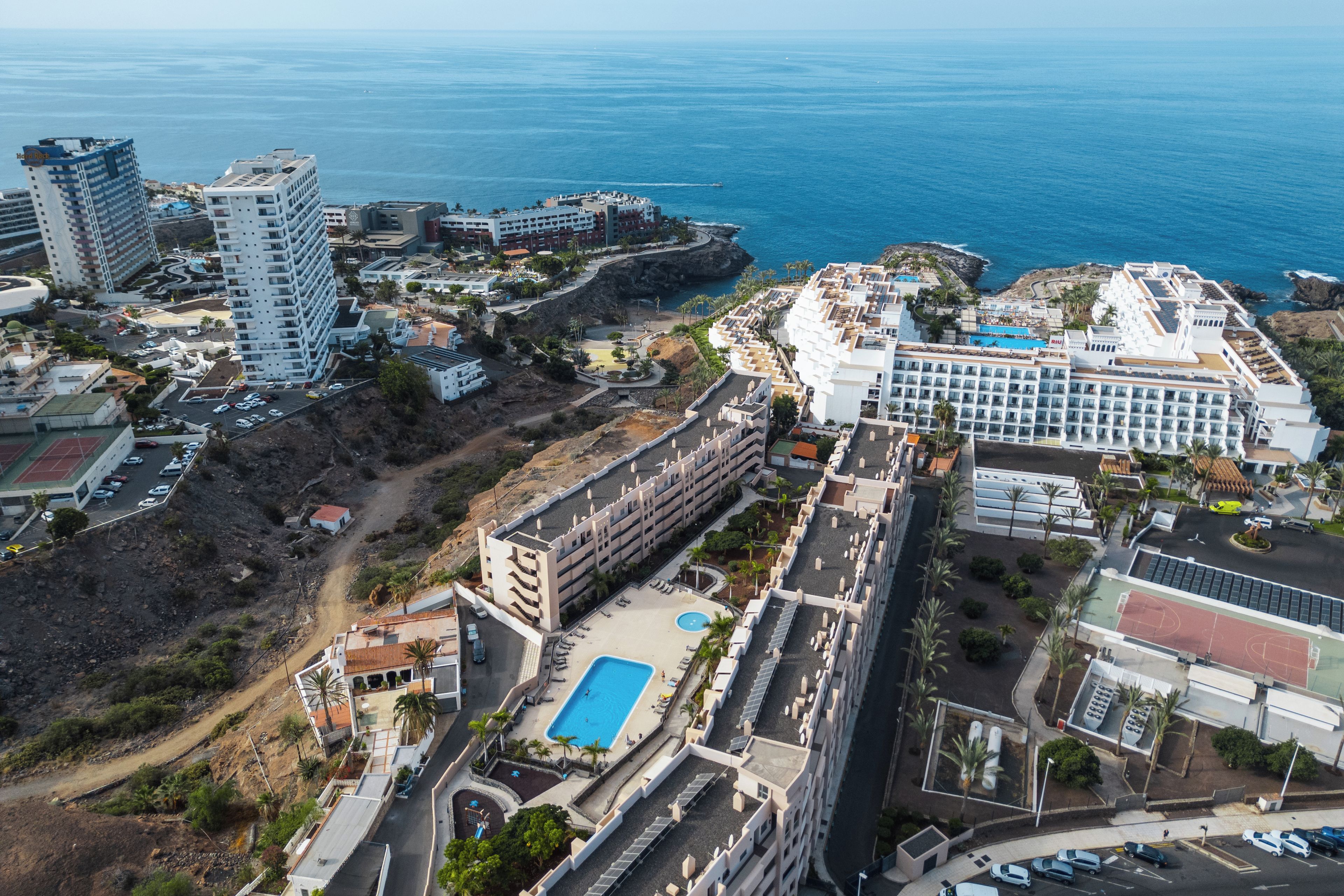 A coastal hotel with multiple buildings, a swimming pool, and a view of the sea.