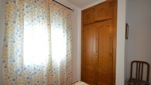 Una stanza con un armadio in legno, una coperta con motivo floreale e una sedia.