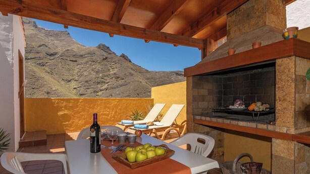 An outdoor patio with a table set for dining, a stone fireplace, and a mountain view. - GC0366 House with heated pool in El Valle de Agaete (Agaete)
