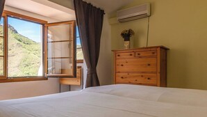 A bedroom with a large bed, a wooden dresser, an open window with curtains, and an air conditioning unit on the wall. - GC0366 House with heated pool in El Valle de Agaete (Agaete)