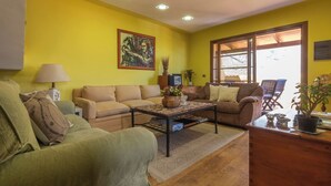 A living room with yellow walls, a green sofa, a brown sofa, a coffee table with a vase of flowers, and a window with a view. - GC0366 House with heated pool in El Valle de Agaete (Agaete)