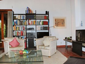 A living room with a bookshelf, two armchairs, a glass coffee table, and a television.