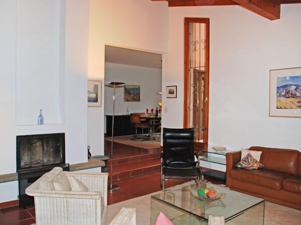 A living room with a glass coffee table, a brown leather sofa, a black chair, and a fireplace.