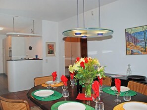 A dining area with a round table set for four, featuring green placemats, white plates, and red napkins. A vase with flowers is centered on the table. - Casa Riva by Interhome (Figino)