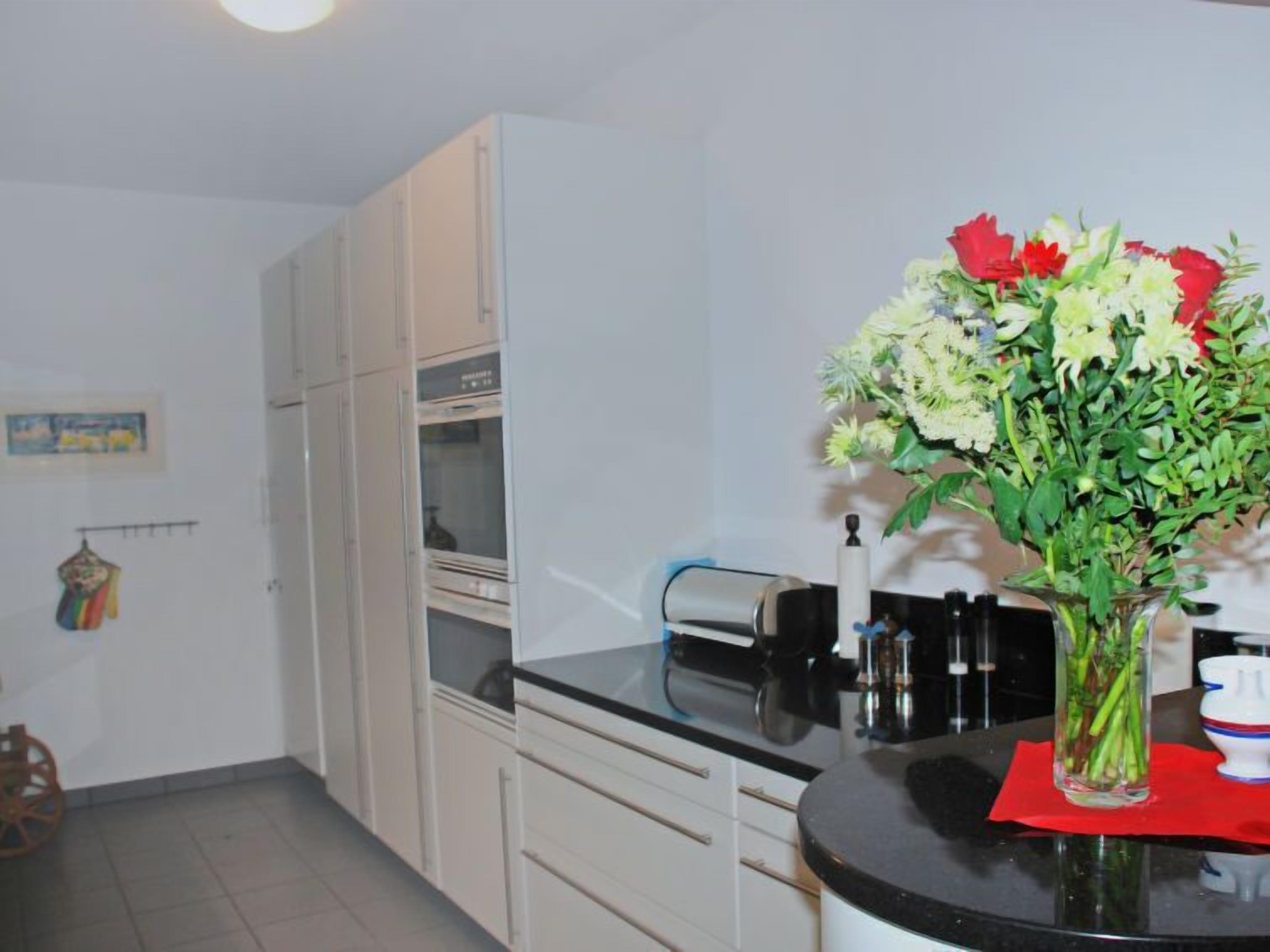 A kitchen with white cabinets, a black countertop, and a vase with flowers on the counter.