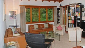 A cozy living room with a brown leather sofa, a glass coffee table, and a bookshelf filled with books. - Casa Riva by Interhome (Figino)