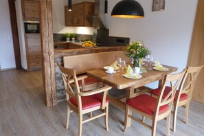 A dining area with a wooden table set for four, red cushioned chairs, a wooden bench, and a potted plant.