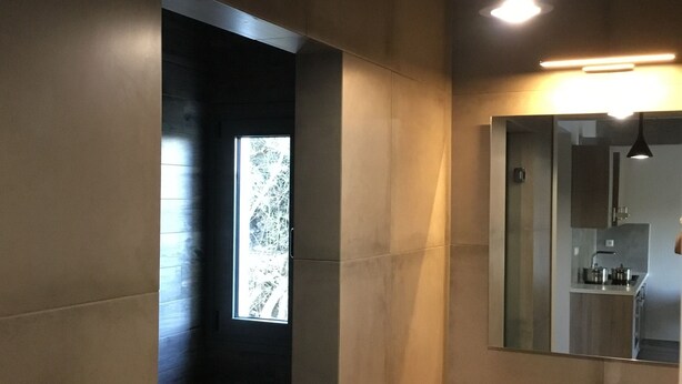 Un baño moderno con un tocador de madera, un lavamanos redondo y un espejo encima. Hay una ventana que proporciona luz natural y vistas a árboles.