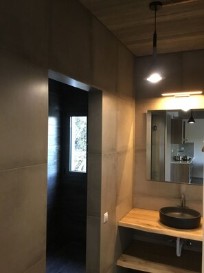 A modern bathroom with a wooden vanity, a round sink, and a mirror above it. There is a window providing natural light and a view of trees outside. - Lagkada Suites (Lefkada)