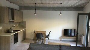 Una cocina moderna con estufa integrada, una zona de comedor con mesa y sillas, un sofá gris y un televisor en una habitación separada.