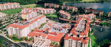A large hotel complex with multiple buildings, a central courtyard, and a lake in the background.