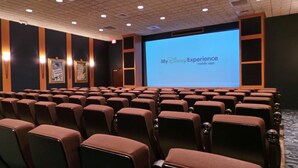 Een vergaderzaal met rijen stoelen gericht op een groot scherm waarop de mobiele app 'My Disney Experience' wordt getoond.