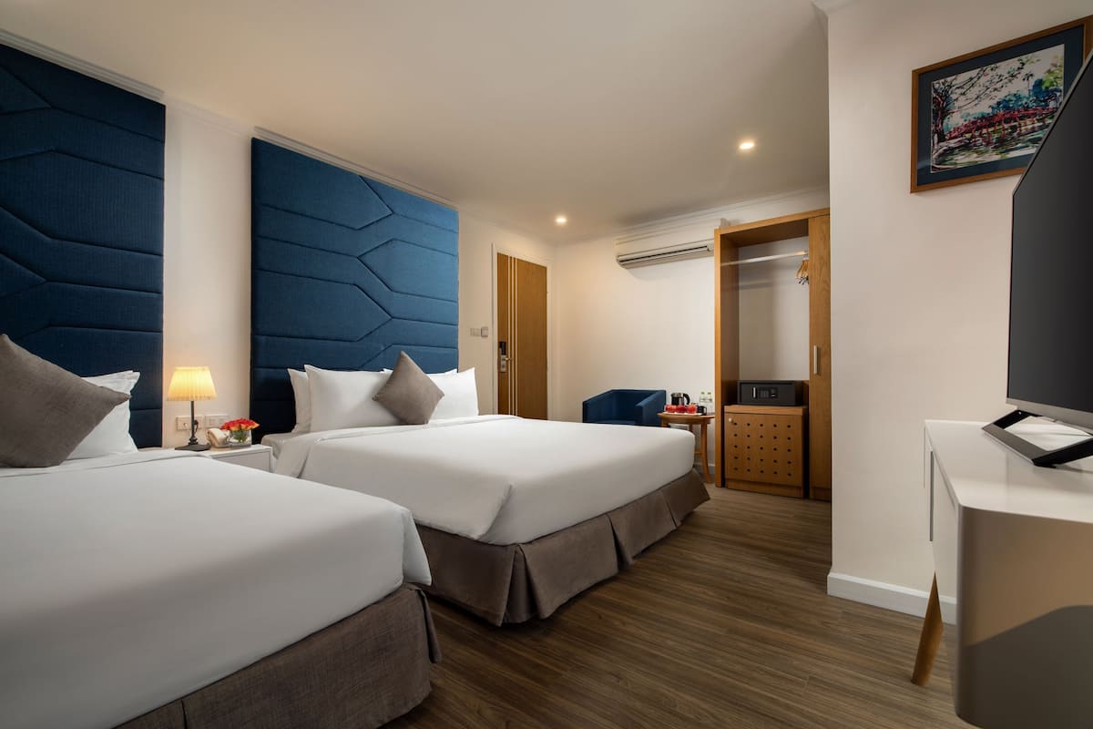 A hotel room with two beds, a desk, a chair, and a wardrobe.