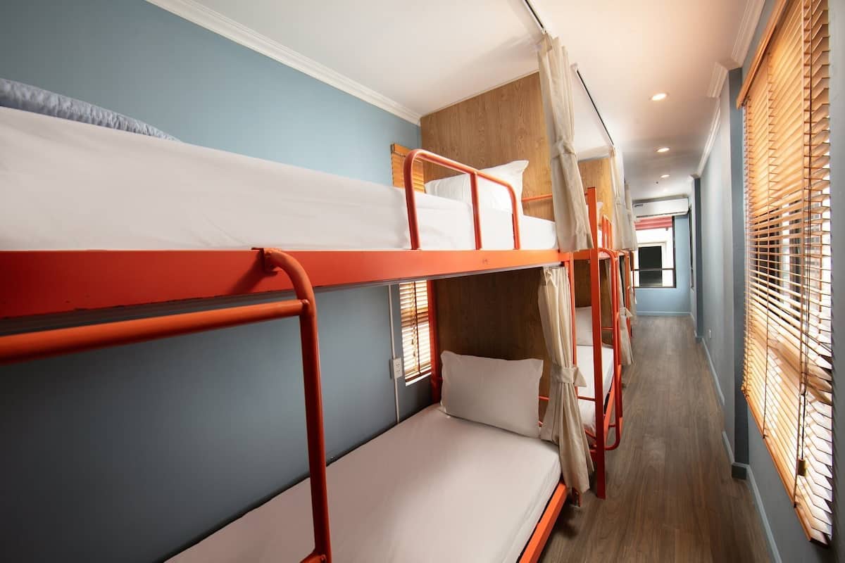 A bunk bed room with a wooden floor, a window with blinds, and a hallway leading to another room.