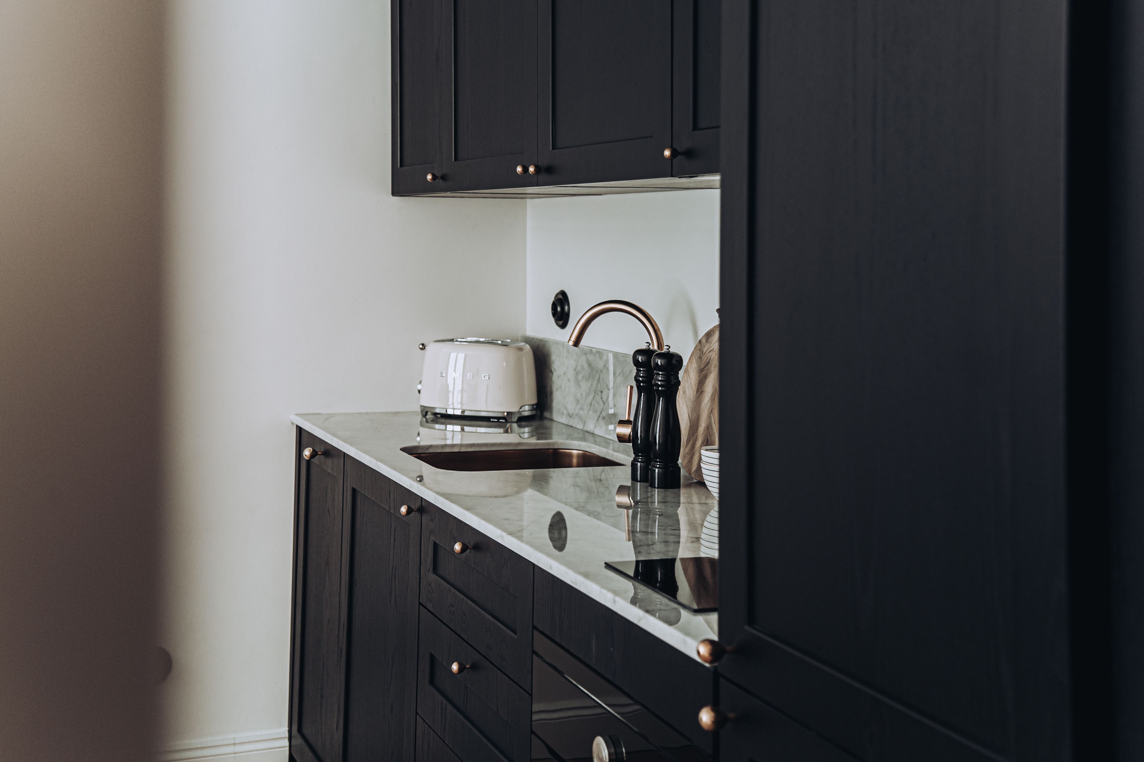 A kitchen with dark cabinets, a white countertop, a toaster, a kettle, and a sink.