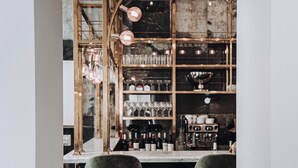 A bar area with two bar stools, shelves with glasses and bottles, and a coffee machine. - Ocho Suites & Kitchen (Palma de Mallorca)