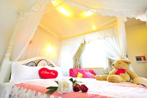 Un dormitorio con cama con dosel, un osito de peluche y un cojín rojo con la frase 'I Love You'.