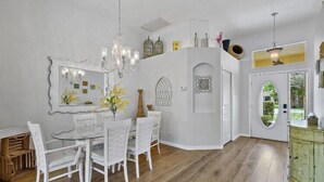 A dining area with a white table and chairs, a chandelier, and a decorative mirror.