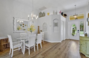 Een eetruimte met een witte tafel en stoelen, een kroonluchter en een decoratieve spiegel.