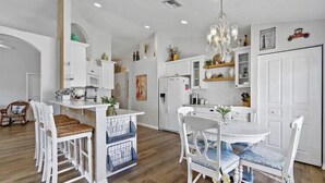 A modern kitchen with white cabinetry, a central island, and a dining area with white chairs.