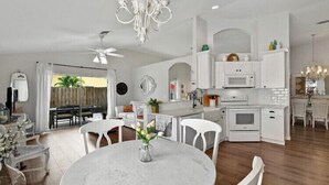 A modern kitchen with white cabinetry, a dining area with a marble table, and a chandelier.