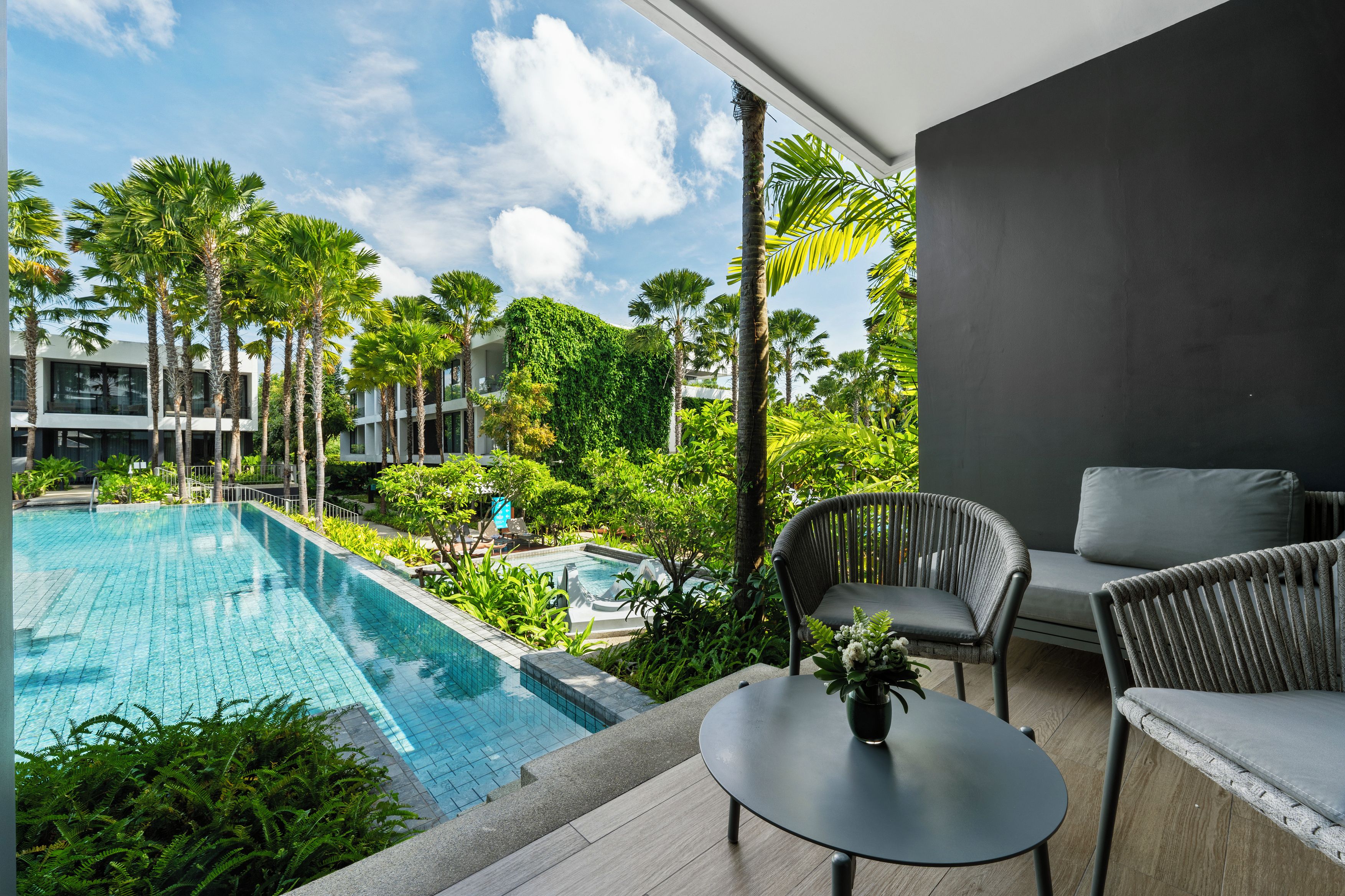A modern hotel balcony with a pool, outdoor seating, and lush greenery.