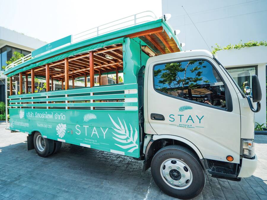 Un autobús STAY verde y blanco con bancos de madera, publicitando un resort con estilo de vida.