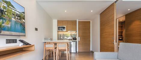 A modern hotel room with a dining area, kitchenette, and a large window overlooking a pool.