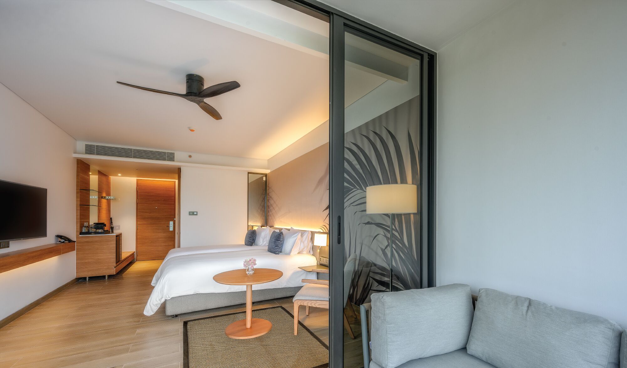 A modern hotel room with a bed, bedside table, lamp, and a TV.
