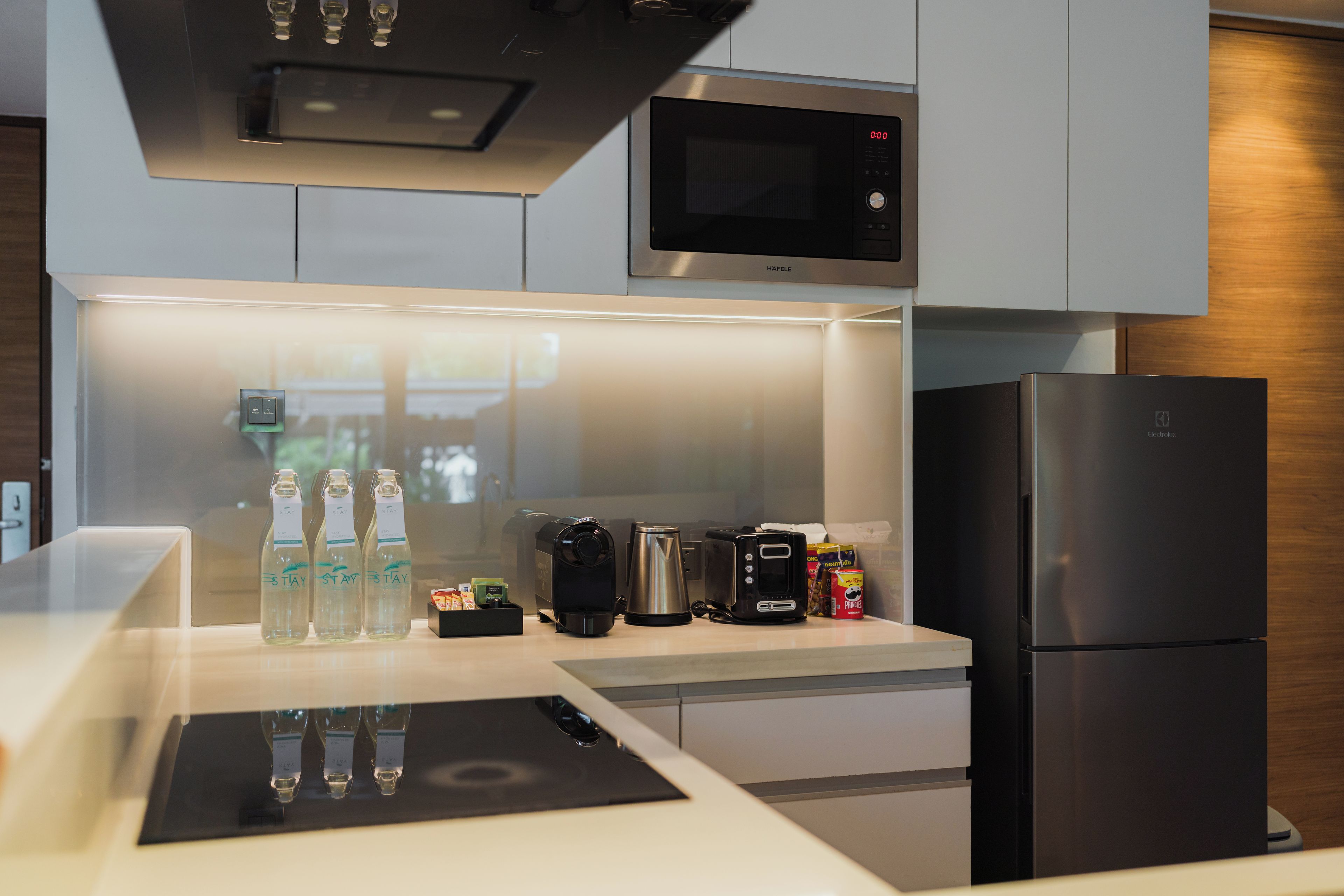 A modern kitchen with a built-in microwave, a refrigerator, a coffee maker, and a kettle.