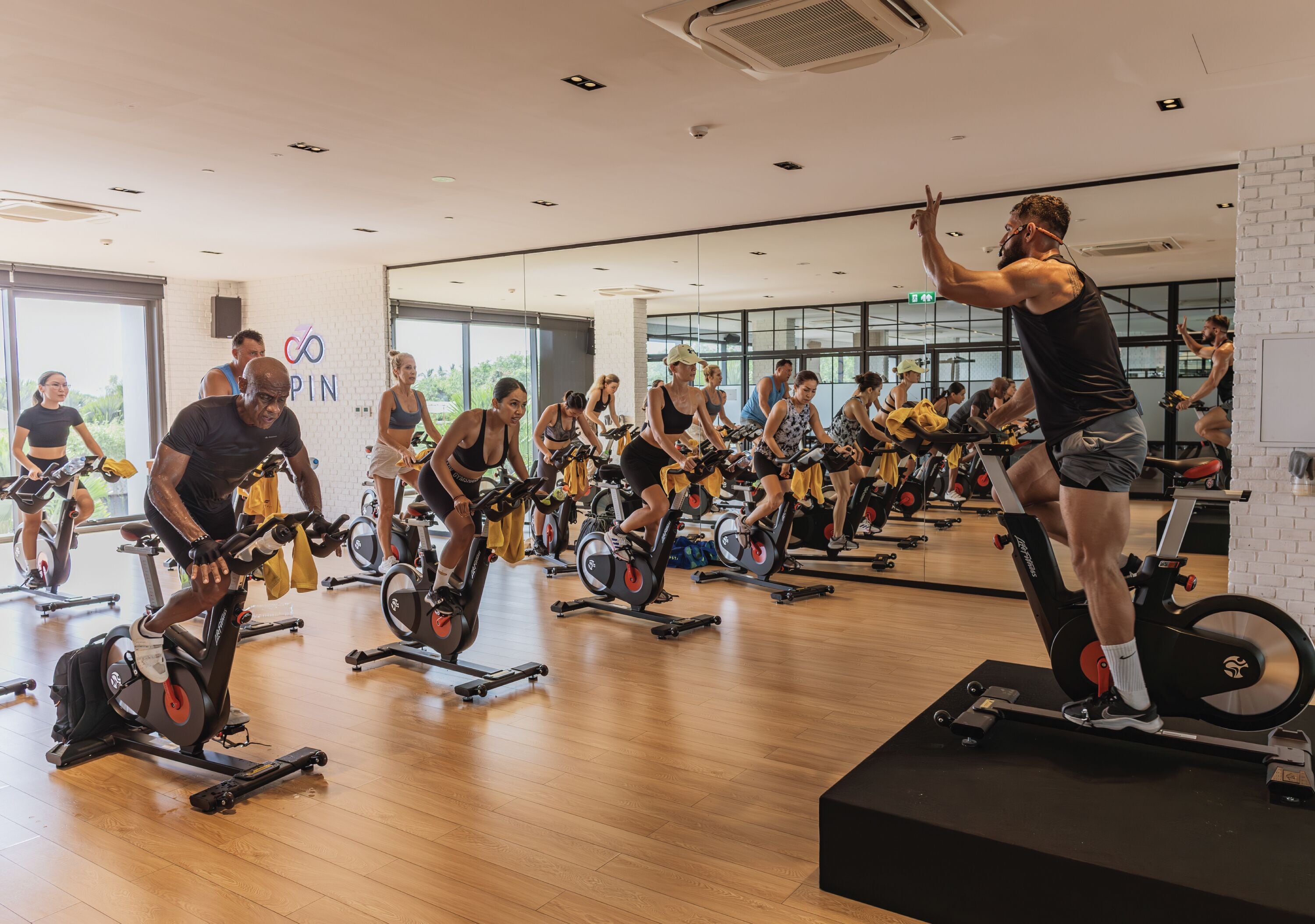 A gym with multiple stationary bikes, a mirrored wall, and a logo on the wall.
