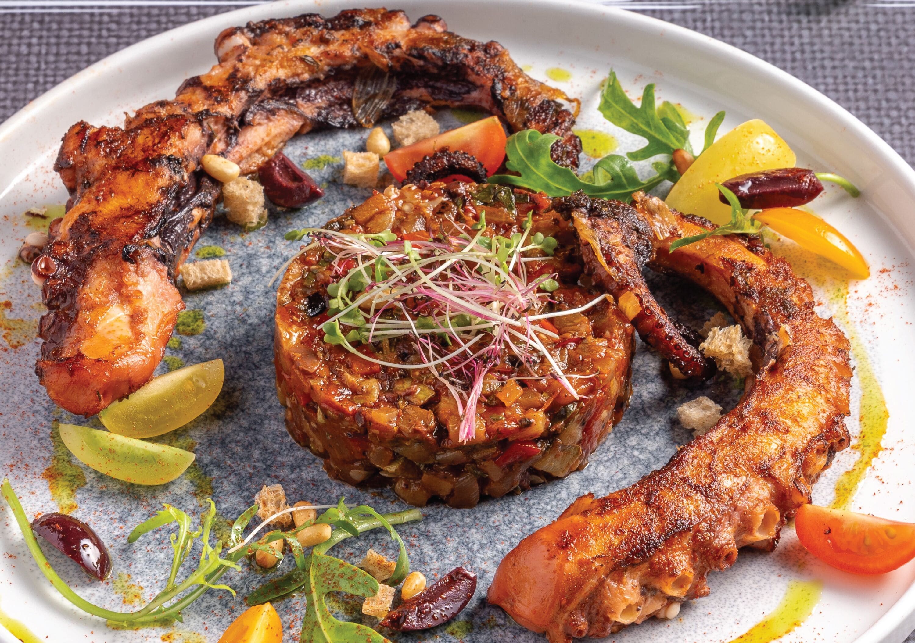 A plate of food with grilled chicken, a stuffed vegetable, and various garnishes.
