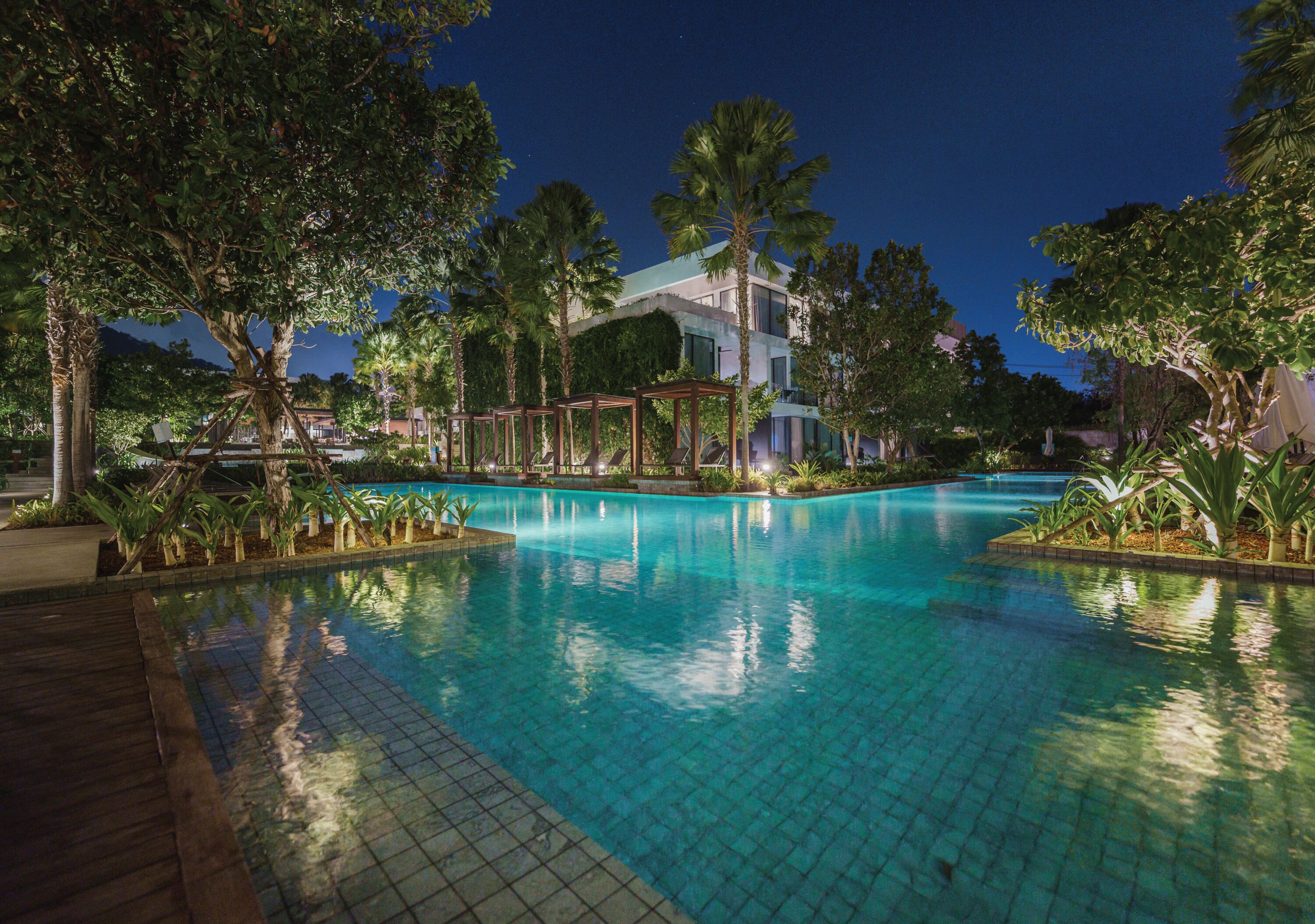 A nighttime swimming pool surrounded by trees and a building.