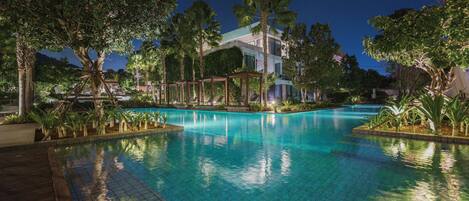 A nighttime swimming pool surrounded by trees and a building.