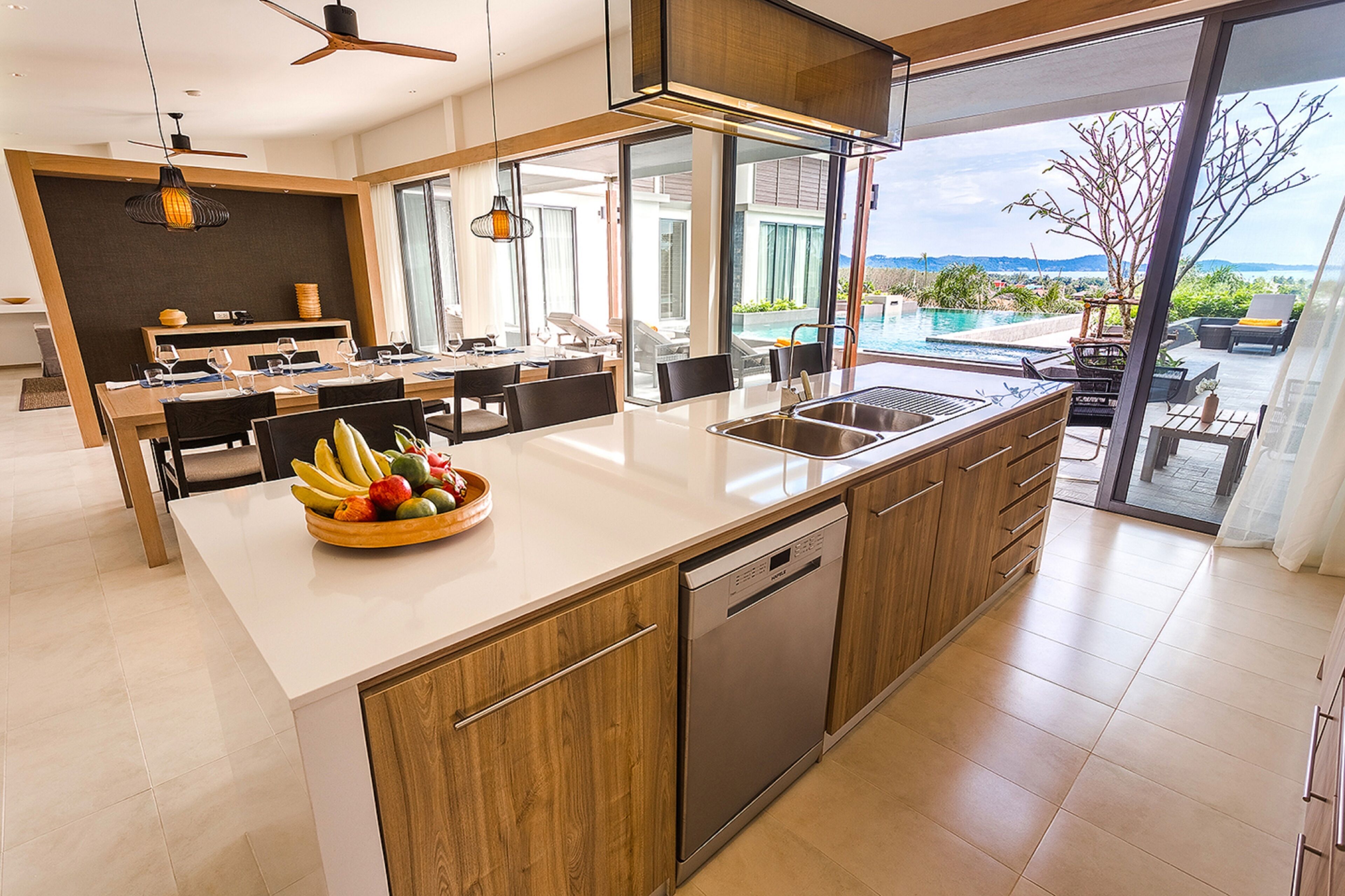 A modern kitchen with a large island, a dishwasher, and a view of a pool and mountains.