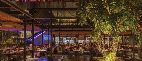 An outdoor dining area with tables and chairs, a water feature, and a covered seating area with plants.