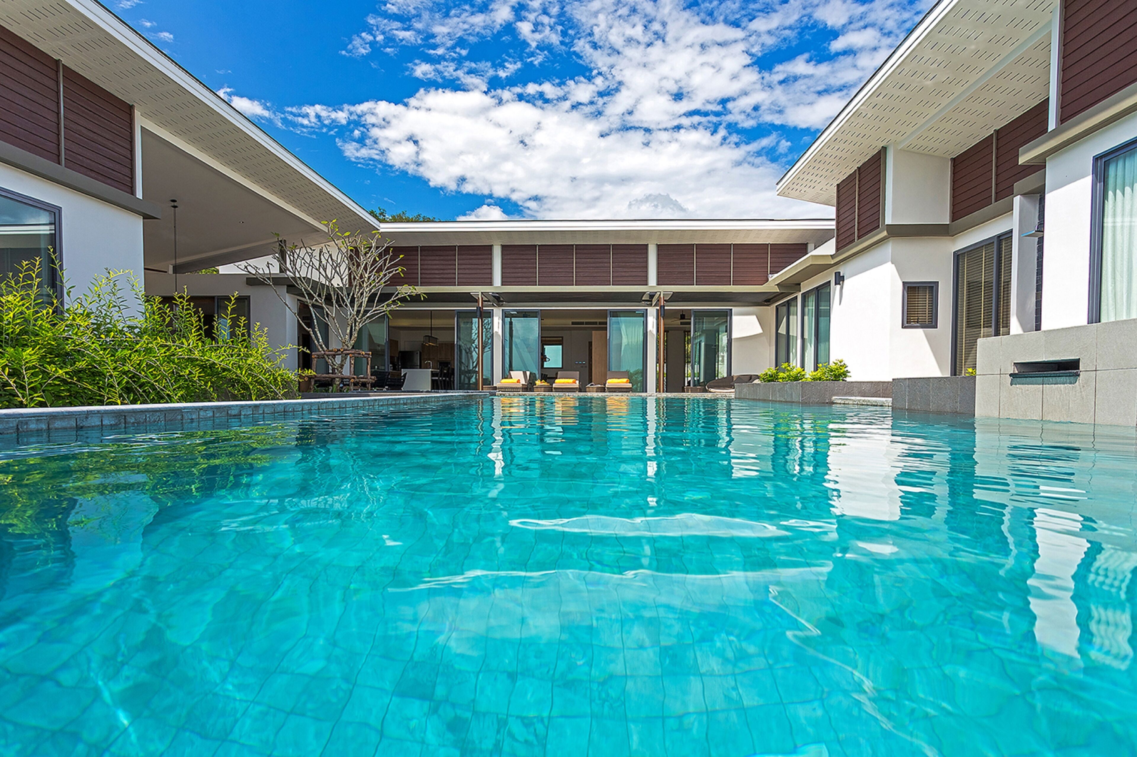 A modern pool area with clear blue water, surrounded by a building with large windows and a covered seating area.