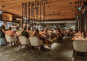 A modern restaurant interior with wooden ceiling panels, tables with candles, and a bar area in the background. - Stay Wellbeing & Lifestyle Resort (Rawai)