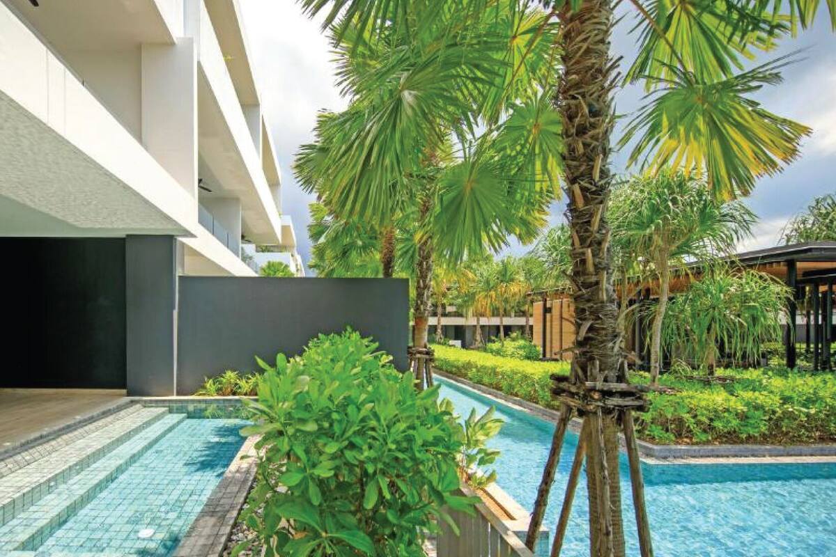 A modern hotel with a pool area, including a lounge with a table and chairs, surrounded by lush greenery and palm trees.