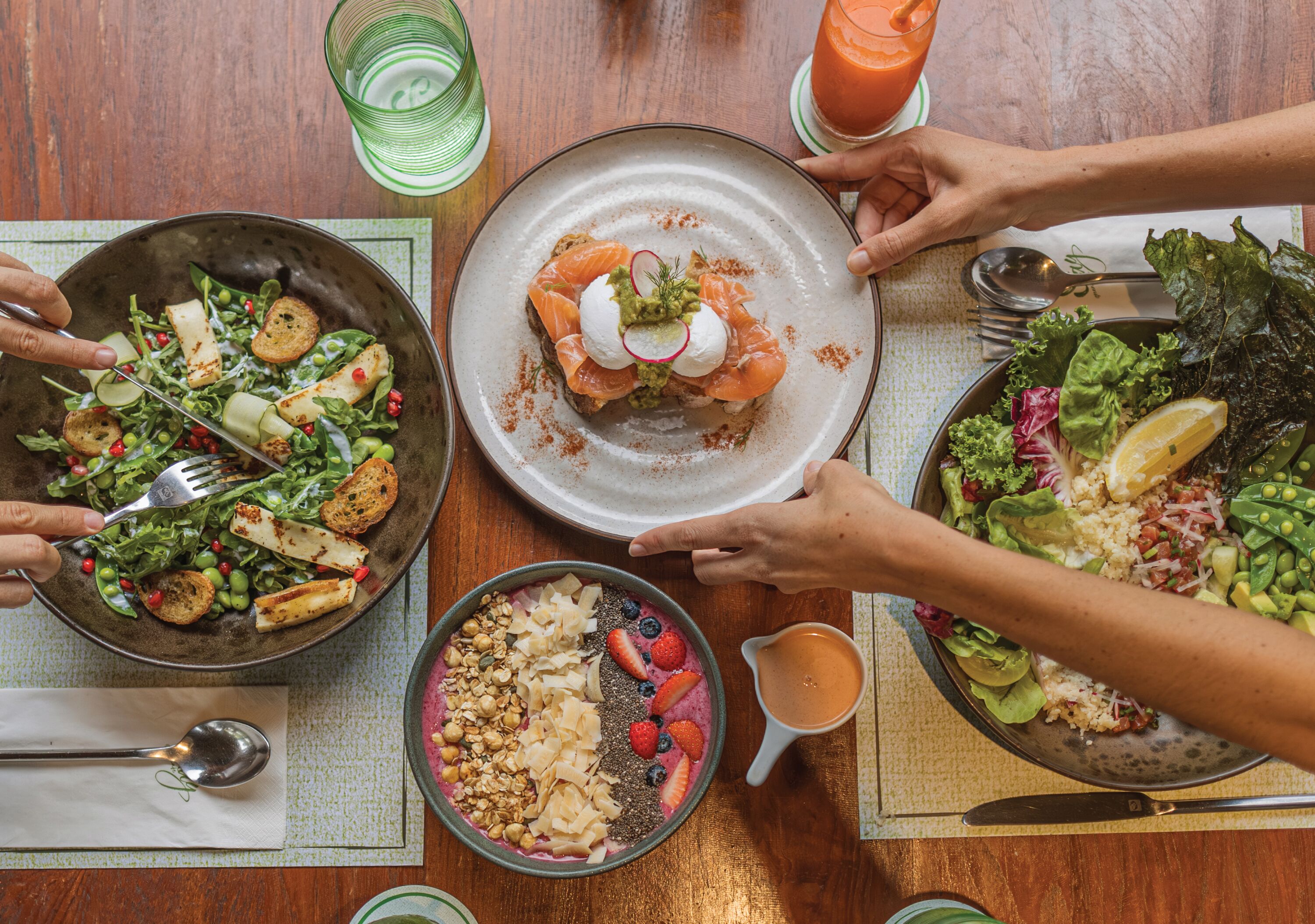 A dining table with various dishes, including a salad, a smoothie, and a bowl of granola.