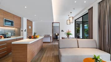 Una cocina moderna con microondas, frutero y mueble de madera. Hay un sofá y una mesa de comedor con un jarrón de flores.