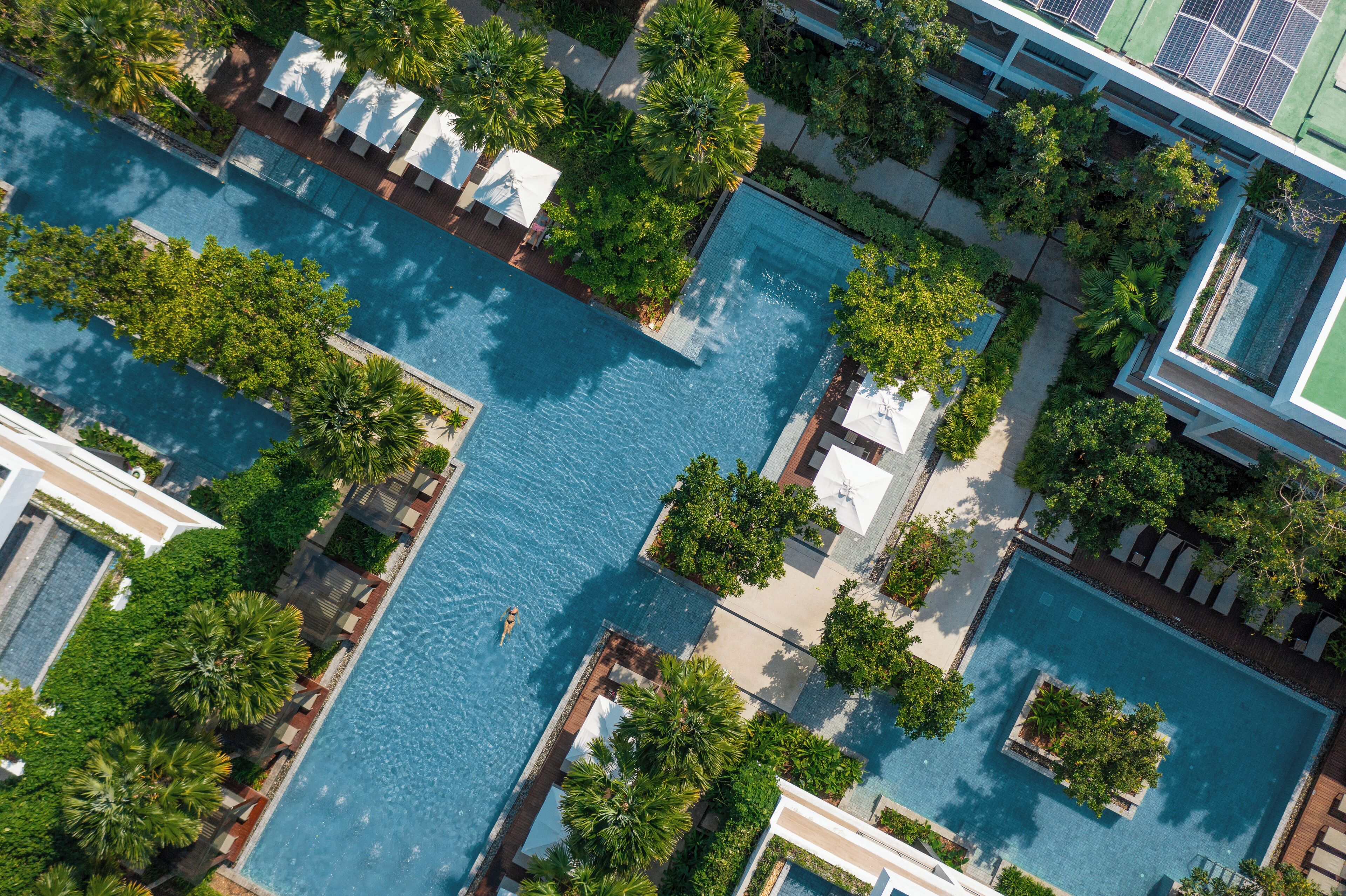 An aerial view of a resort with multiple swimming pools surrounded by lush greenery and shaded areas.