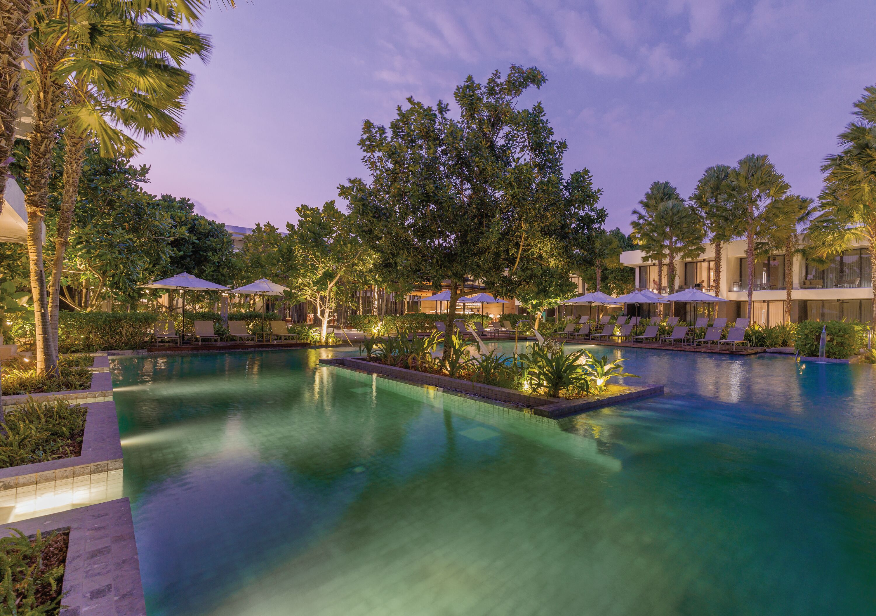 A pool area with lounge chairs and umbrellas, surrounded by palm trees and buildings.